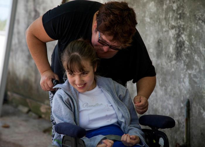 Mujer hablando con niña sentada en silla de ruedas, que se ríe.